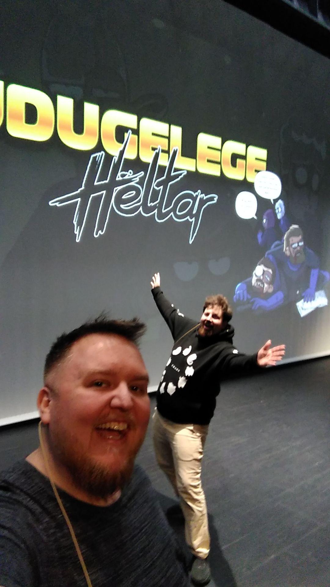 Bilete av to menn på ei scene. Ein av dei er @markus@skvip.lol. Bak dei er ein skjerm med logoen til teikneserien "Udugelege heltar". 

Mannen nærmast kameraet smilar. Mannen bak strekkar armane ut til sidane for å vise fram biletet bak dei.